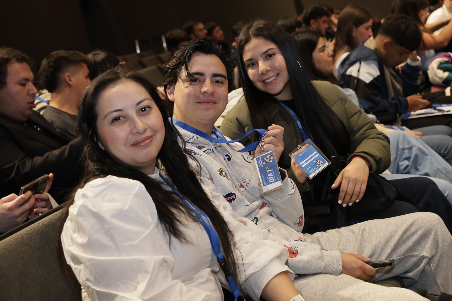 Tres participantes posan desde sus asientos en el auditorio.
