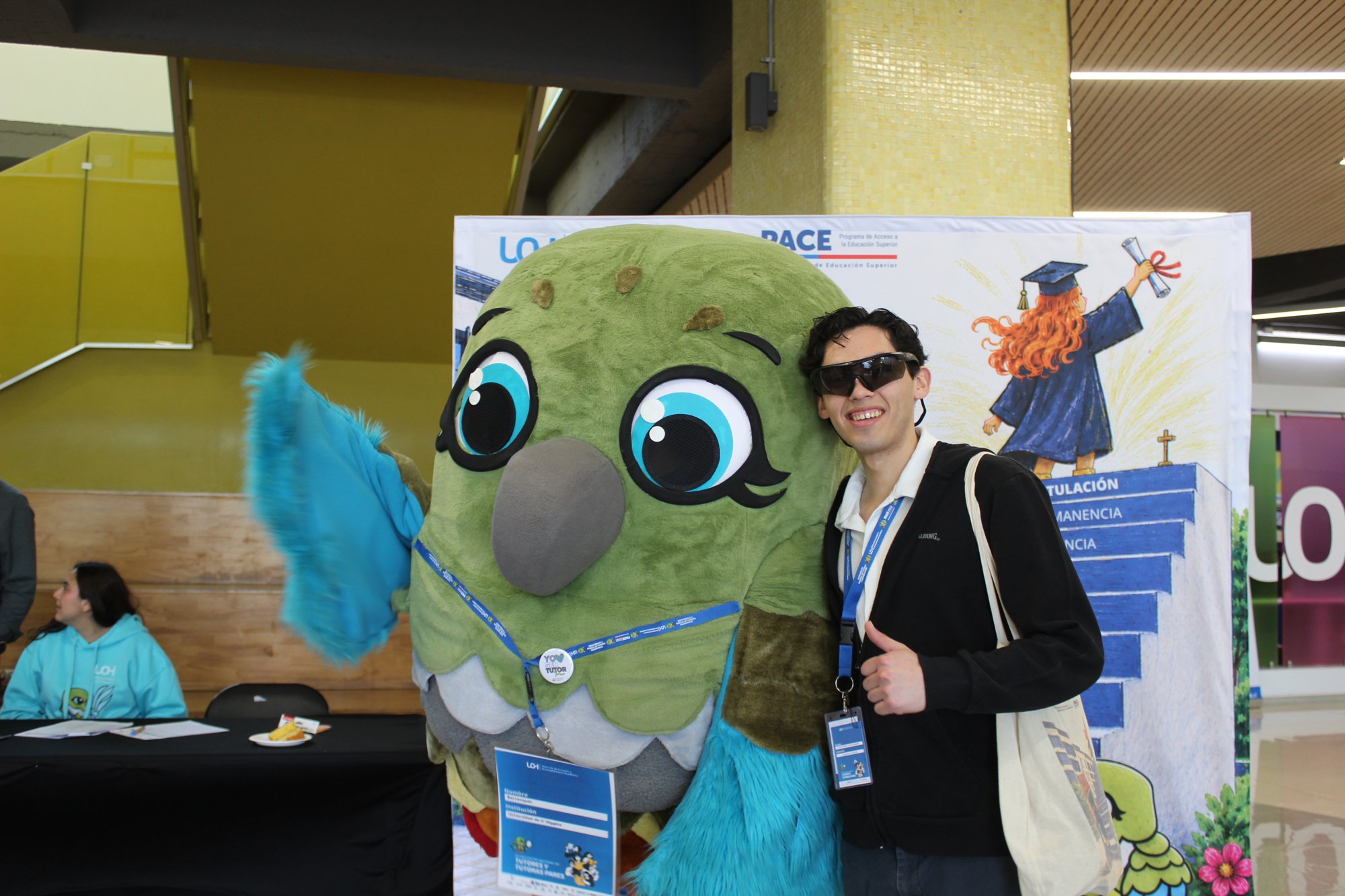 Participante con gafas posa junto a la mascota del encuentro.