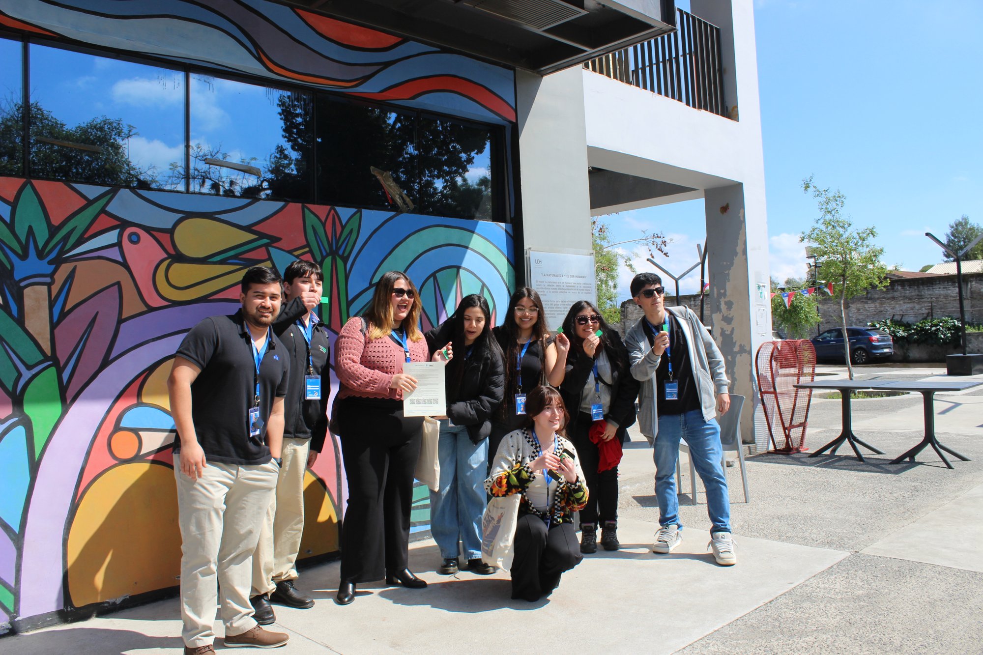 Grupo de participantes posa junto a un mural del campus.