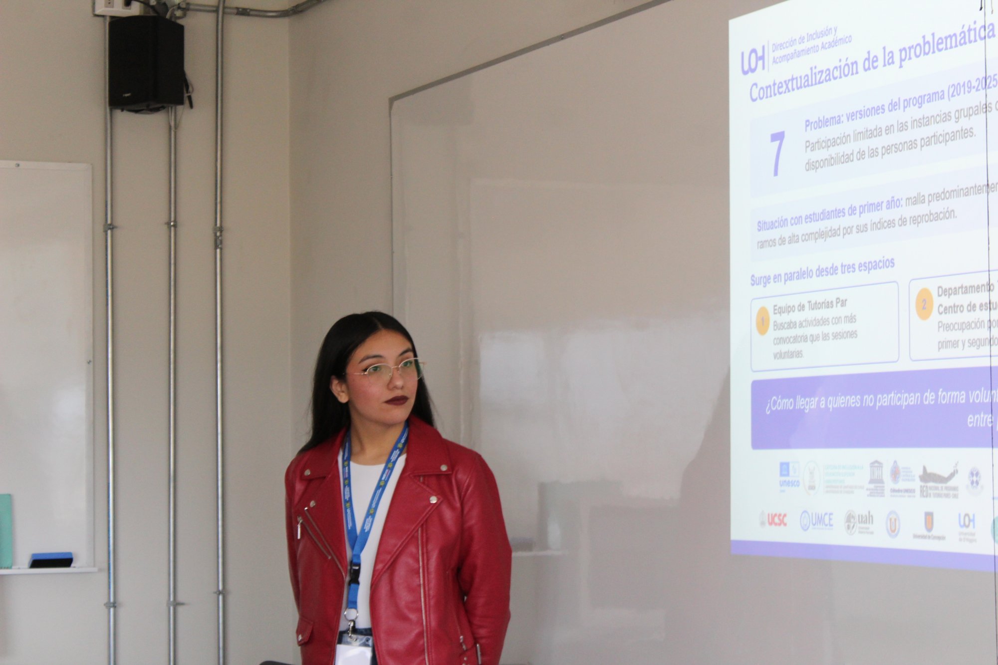 Una expositora presenta su trabajo junto a una proyección.