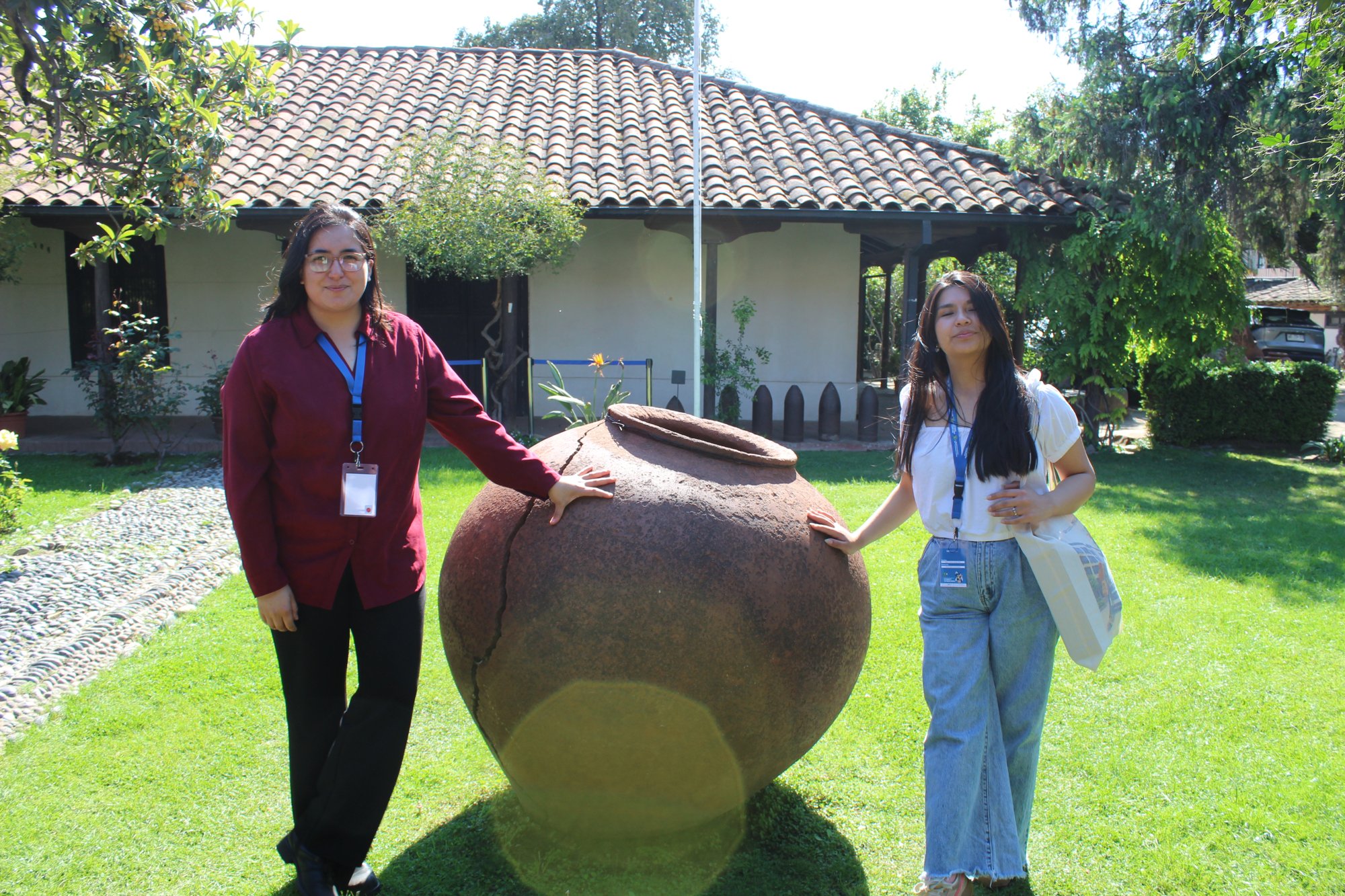 Dos personas posan junto a una gran vasija en un jardín.