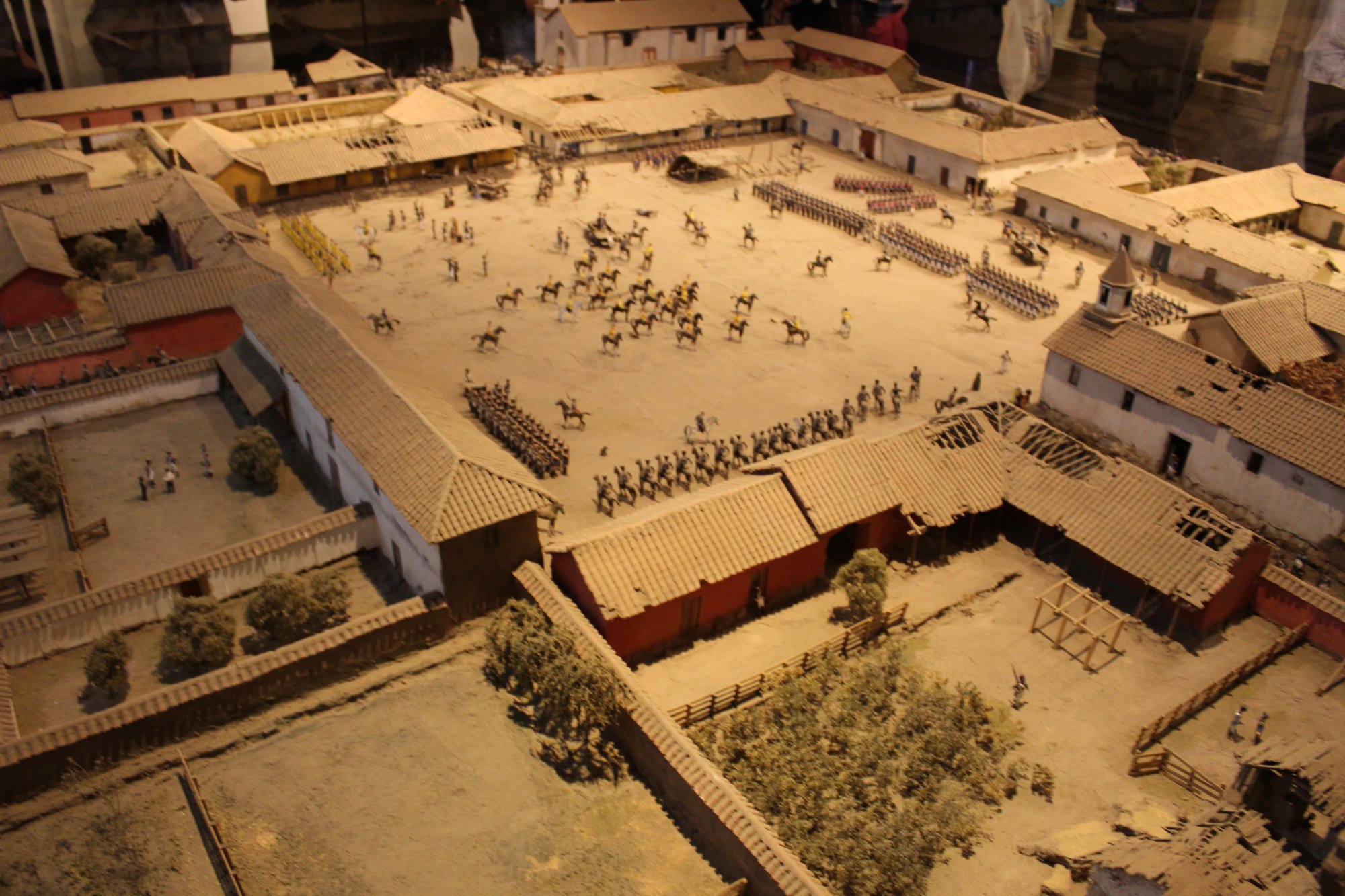 Maqueta con construcciones, calles y pequeñas figuras dentro de una vitrina.