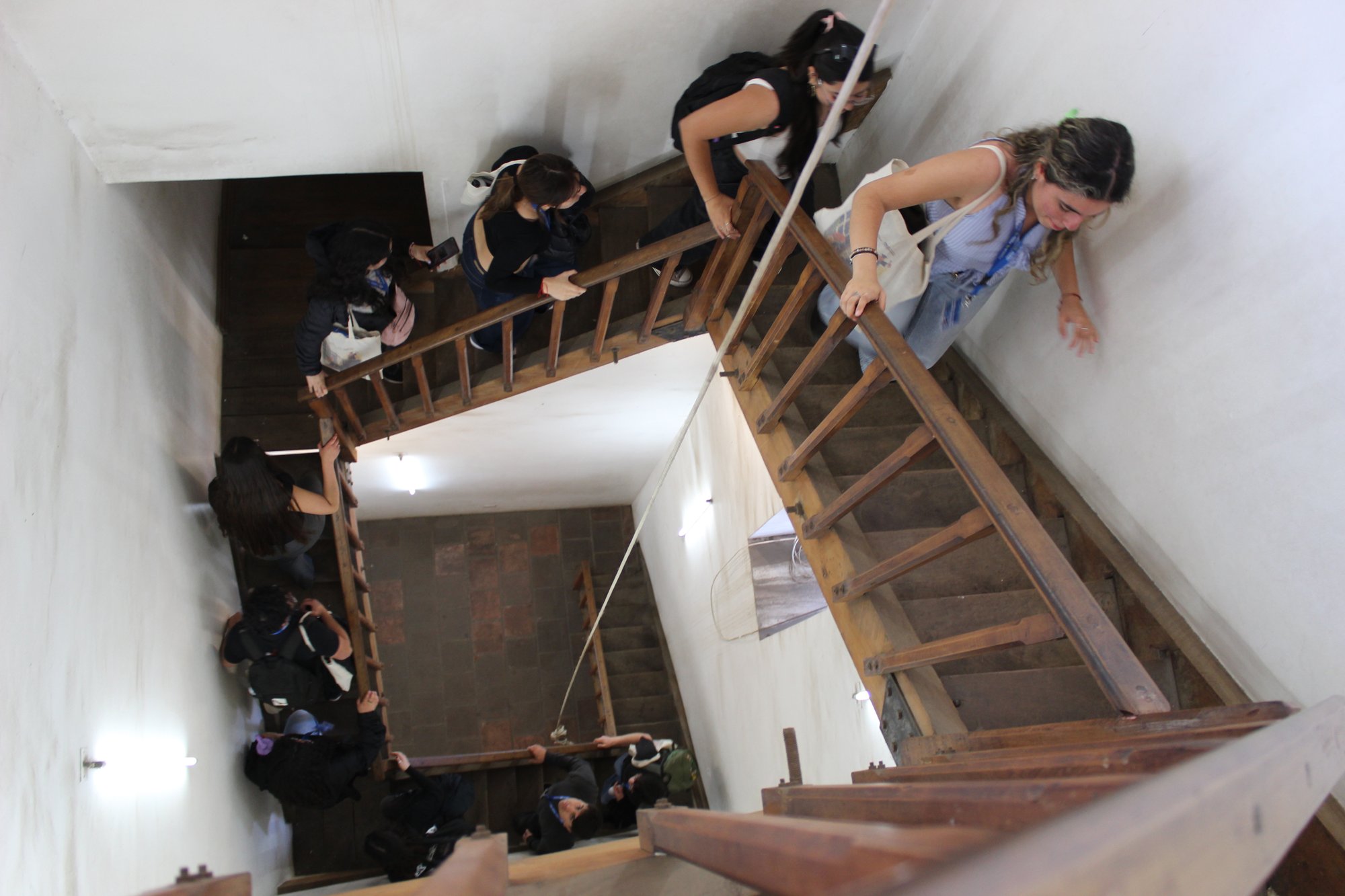 Varias personas recorren una escalera de madera vista desde arriba.