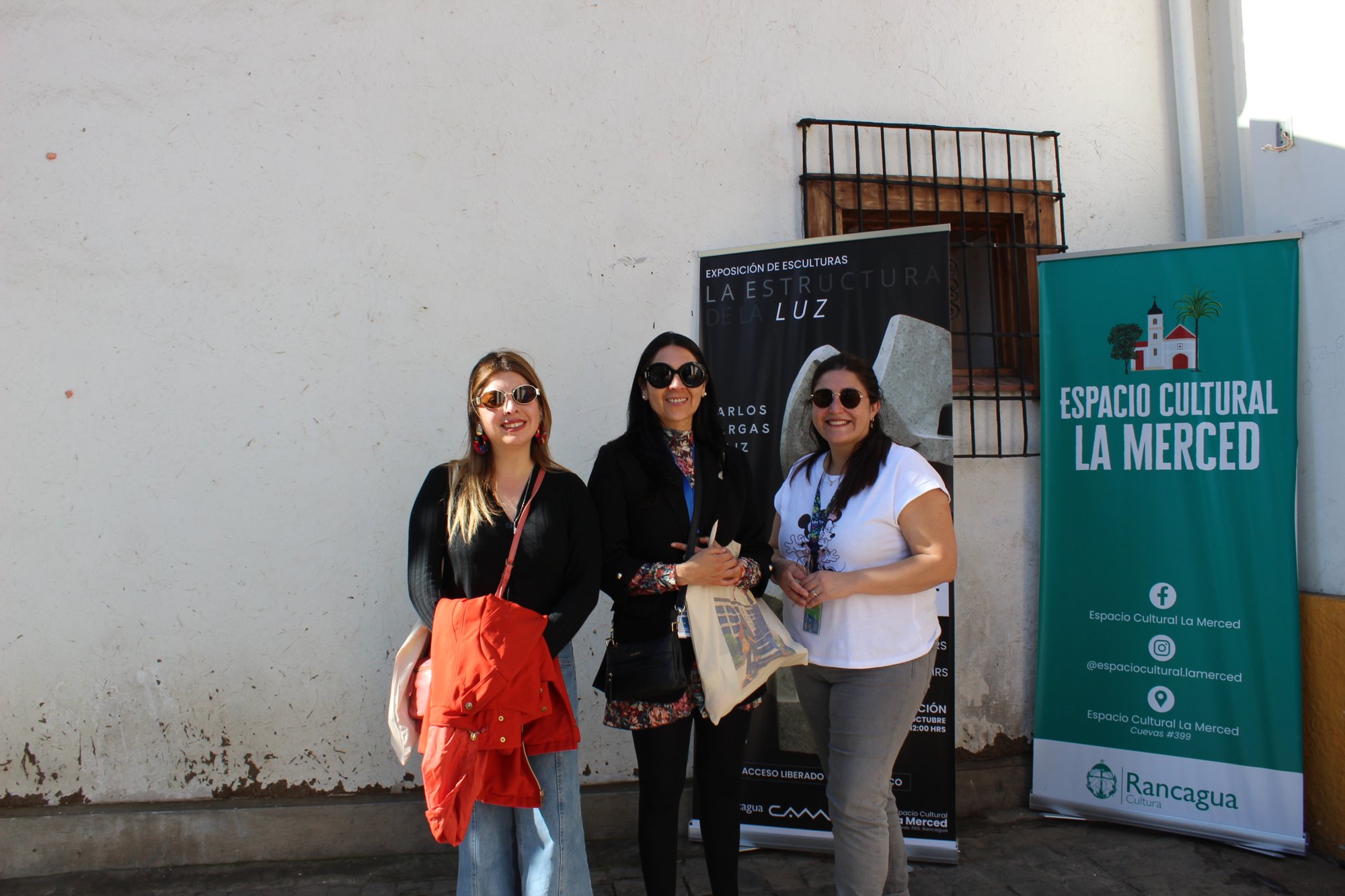 Tres personas posan junto a la entrada de un espacio cultural.