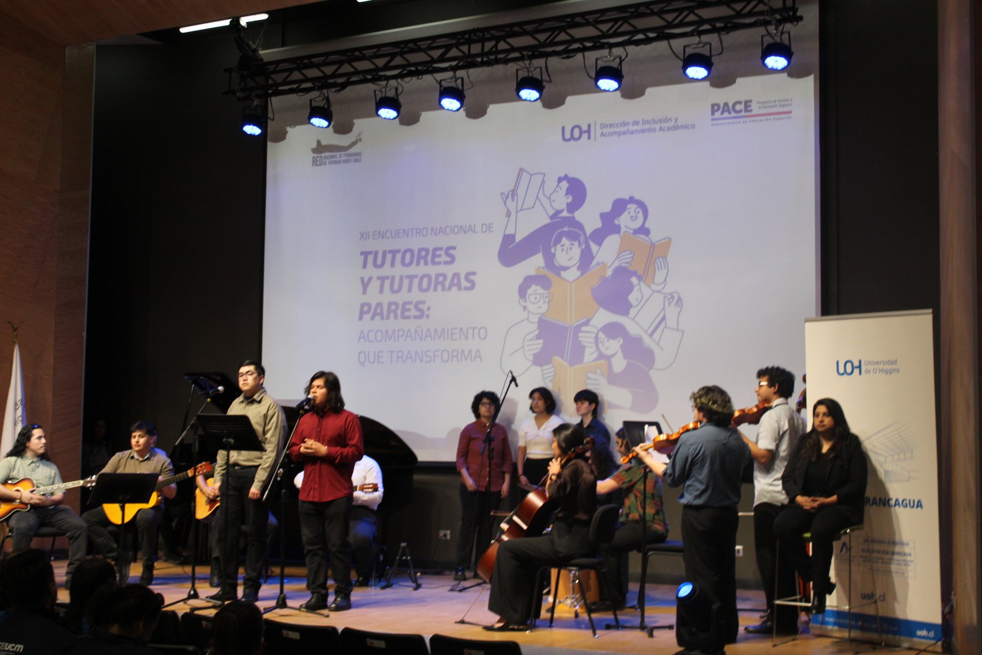 Un conjunto musical se presenta sobre el escenario frente a la pantalla del encuentro.