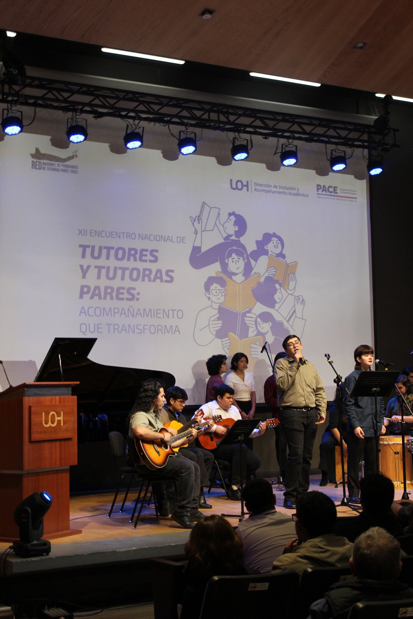 Vista vertical del escenario con un conjunto musical y público en primer plano.