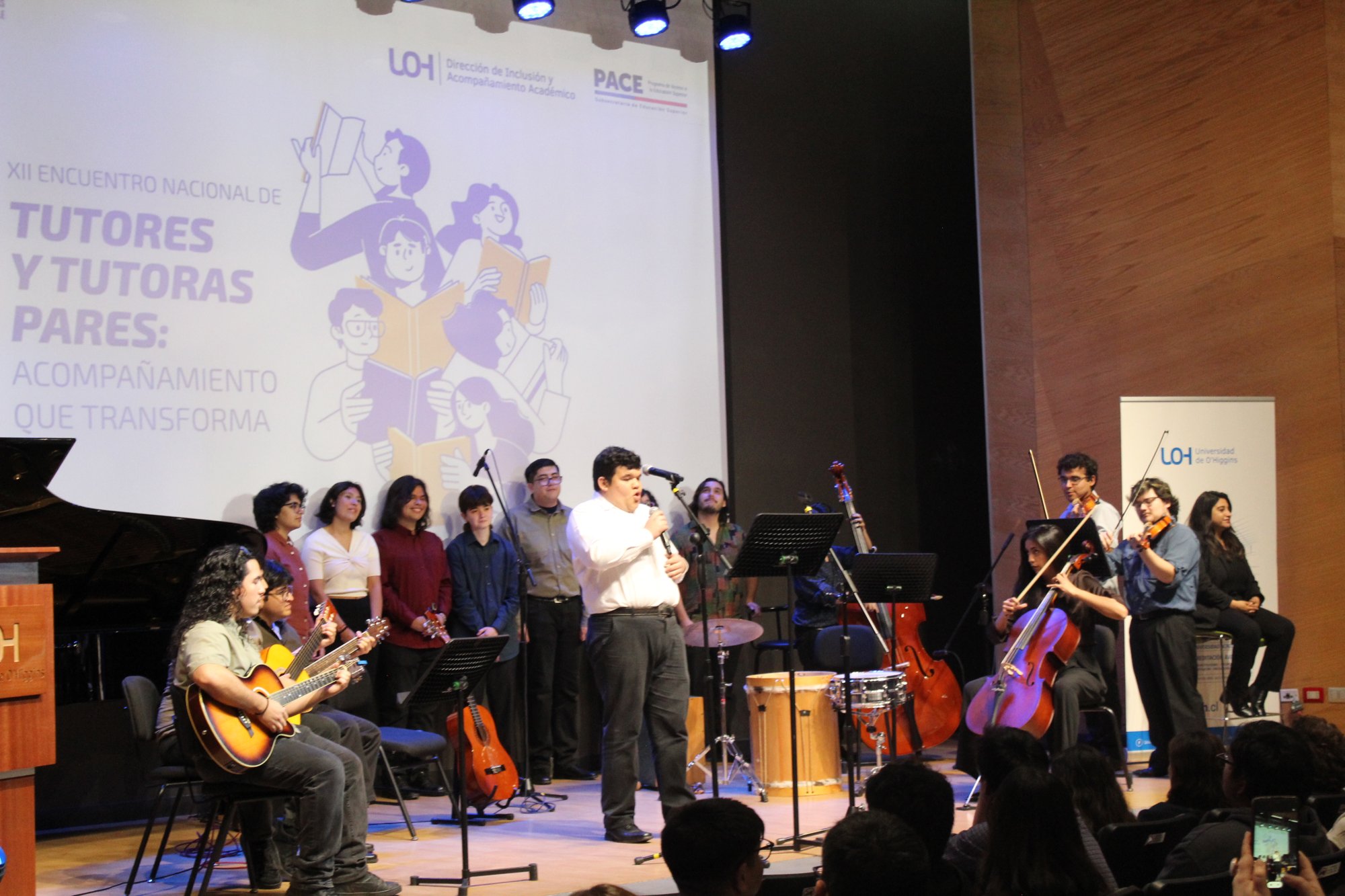 Personas cantan y tocan instrumentos sobre el escenario del auditorio.