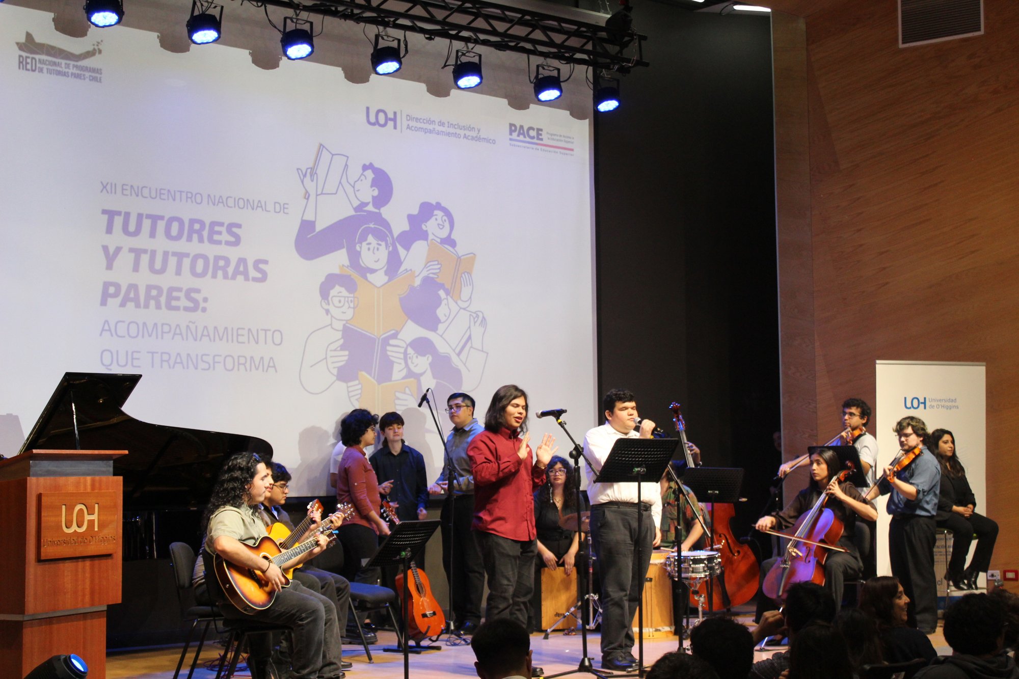 Un conjunto de voces e instrumentos se presenta frente a la pantalla del encuentro.