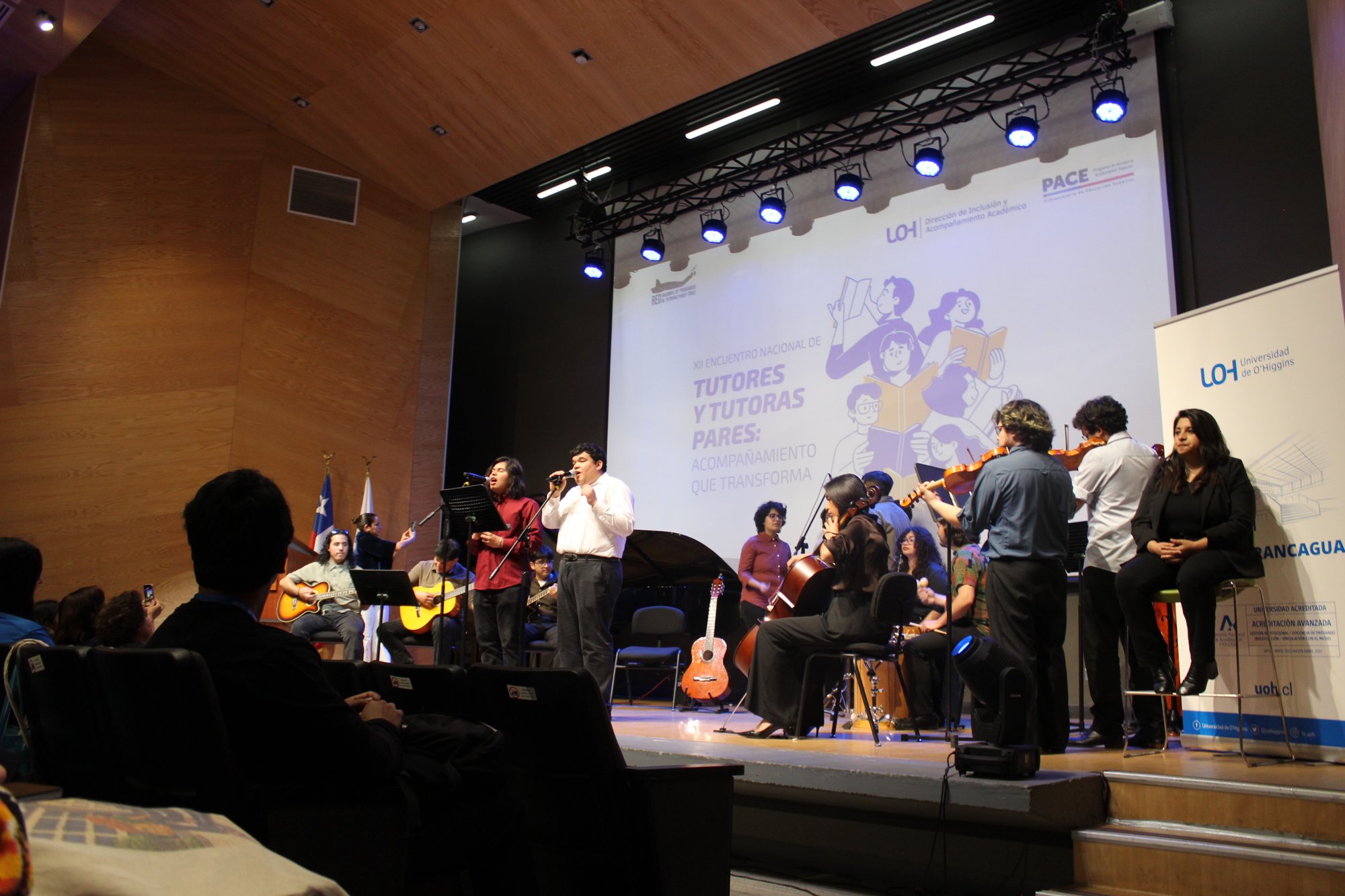 Vista lateral del escenario con integrantes de un conjunto musical.
