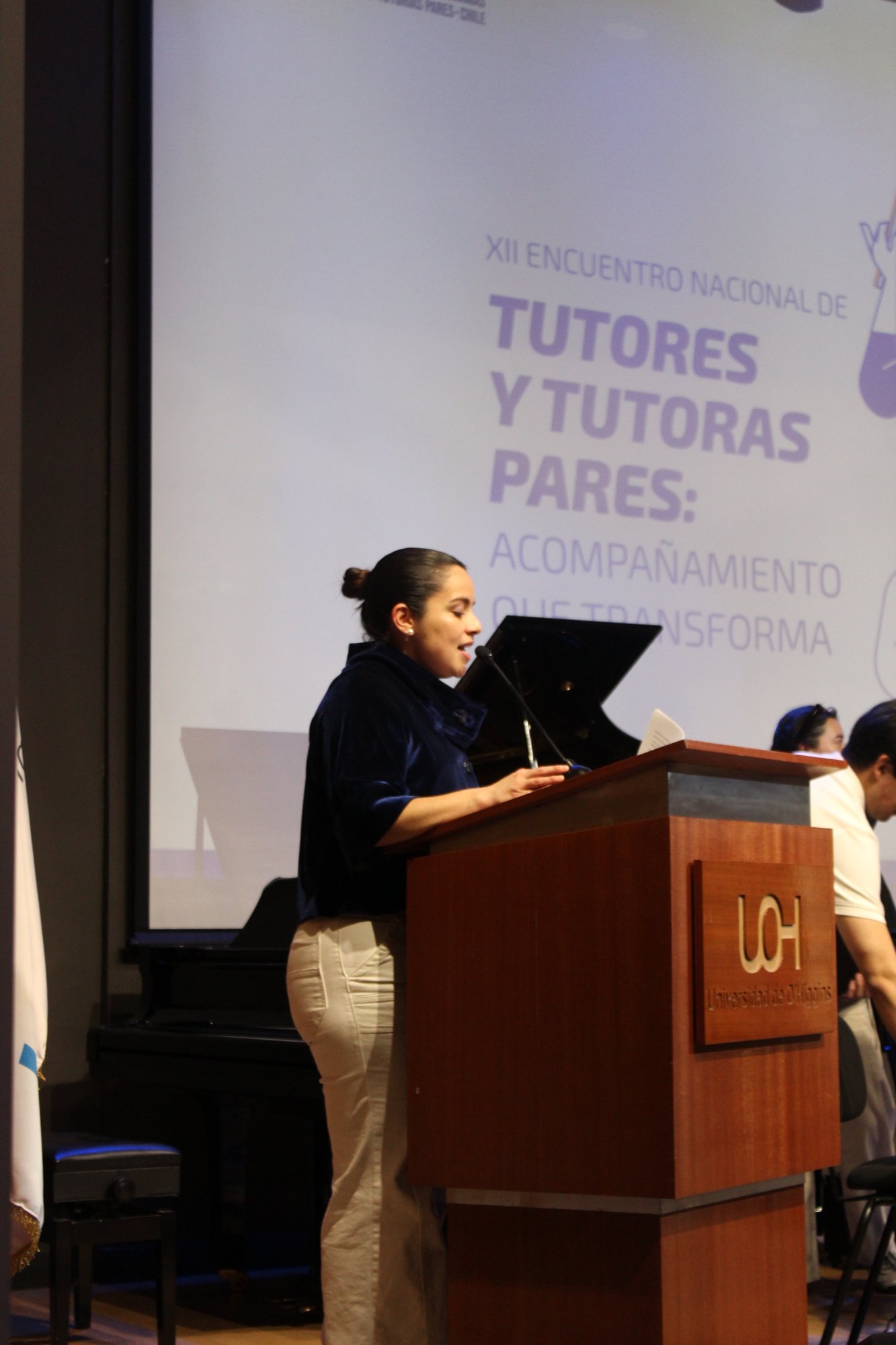 Una persona interviene desde el atril del auditorio con una hoja en las manos.