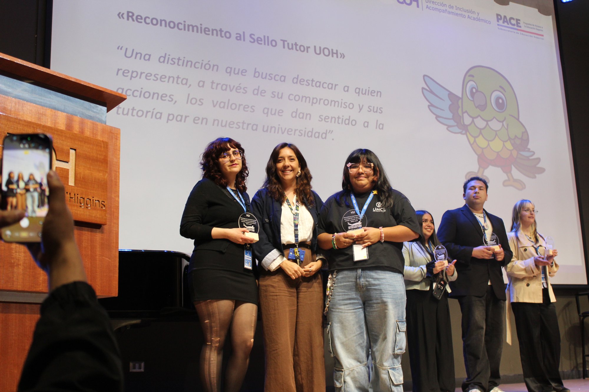 Varias personas posan sobre el escenario mientras alguien las fotografía desde el público.